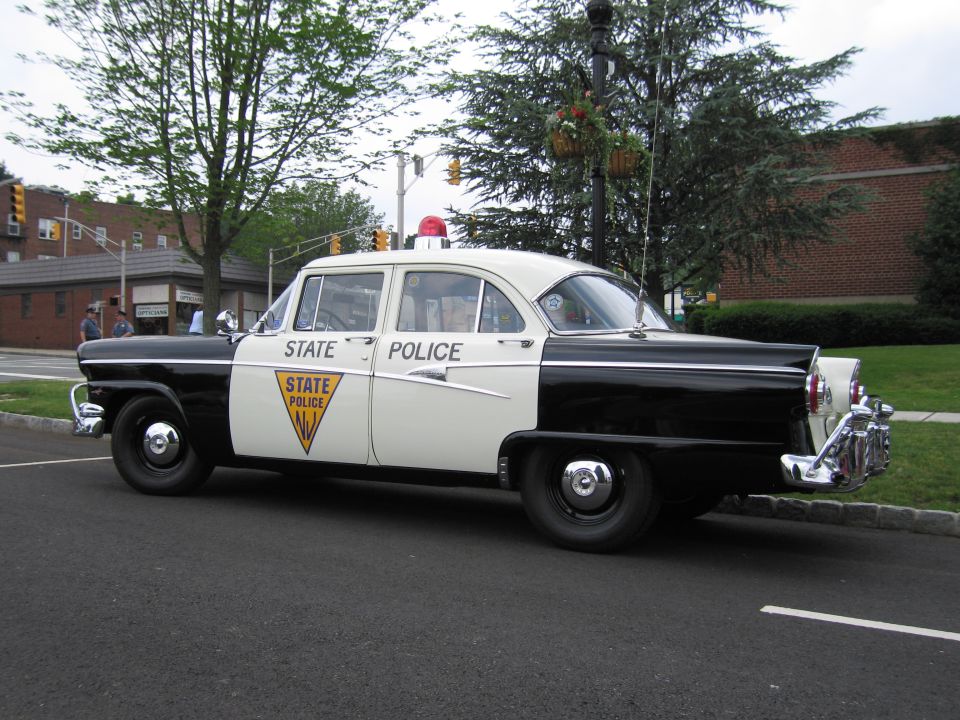 1950s black and white NJ State Police Ford sedan, front three-quarter view at curb