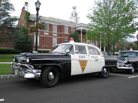 1991 Ford LTD Crown Victoria - 1950s black-and-white New Jersey State Police Ford sedan parked front three-quarter outside a brick municipal building.