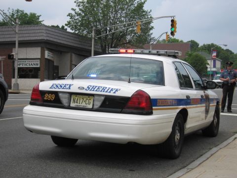 1991 Ford LTD Crown Victoria - white Essex Sheriff Ford Crown Victoria (unit 289) with an illuminated roof lightbar stopped at a street intersection.