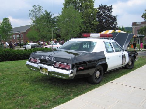 1991 Ford LTD Crown Victoria - black-and-white Plymouth Police sedan with its trunk open and roof lightbar lit, parked rear three-quarter near a walkway.