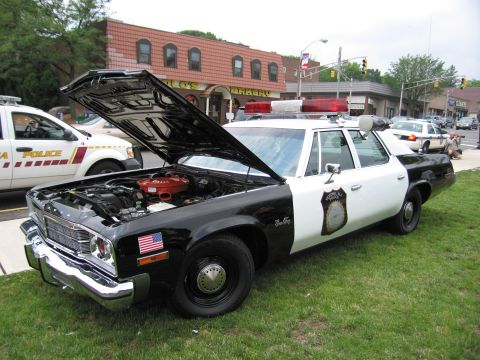 1991 Ford LTD Crown Victoria - black-and-white classic police sedan displayed with hood open, light bar on roof and an American flag decal.