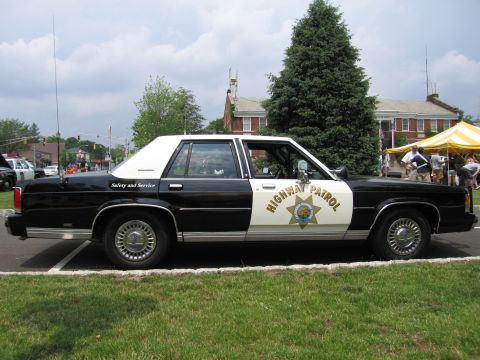 1991 Ford LTD Crown Victoria - Side profile of a black-and-white Ford Highway Patrol sedan marked Safety and Service with a star shield.