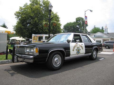 1991 Ford LTD Crown Victoria - Front three-quarter view of a black-and-white Ford Highway Patrol sedan parked near vendor tents.