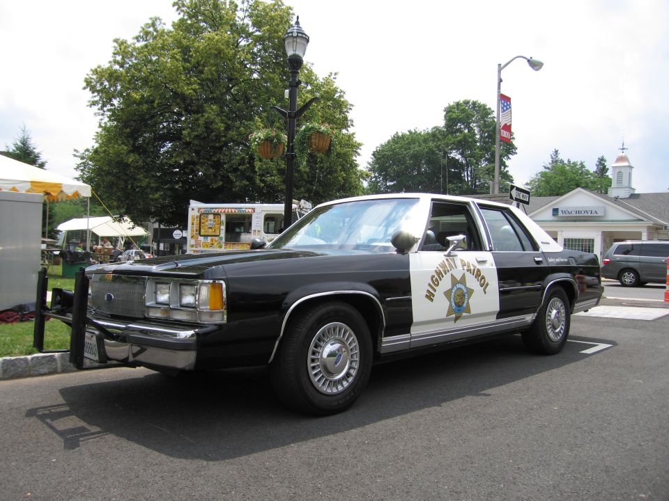 Black-and-white Ford Highway Patrol sedan front three-quarter at outdoor event