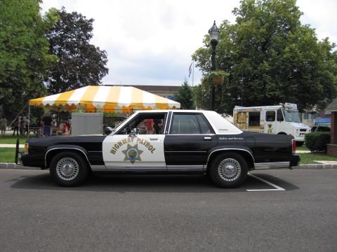 1991 Ford LTD Crown Victoria - Side view of a black-and-white Highway Patrol sedan with star shield, parked at a community event.