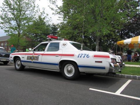 1991 Ford LTD Crown Victoria - white State Police sedan numbered 1776 with red and blue stripes and a roof light bar, rear view.