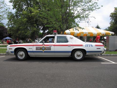 1991 Ford LTD Crown Victoria - Side profile of a white State Police sedan numbered 1776 with red and blue stripes and roof light.