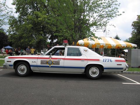 1991 Ford LTD Crown Victoria - White State Police sedan numbered 1776 shown in profile with onlookers and tents in the background.