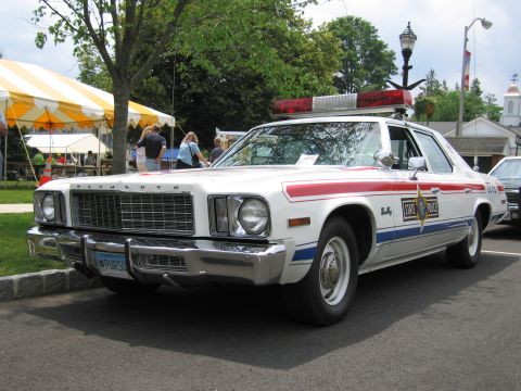 1991 Ford LTD Crown Victoria - Front three-quarter of a white Plymouth State Police sedan with red-white-blue stripes and roof light bar.