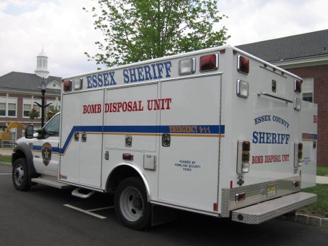 1991 Ford LTD Crown Victoria - white Essex County Sheriff Bomb Disposal Unit box truck with blue and orange striping, parked in a lot beside a brick building.
