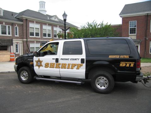 1991 Ford LTD Crown Victoria - Driver-side profile of a black-and-white Passaic County Sheriff Mounted Patrol Ford Excursion SUV parked on a street.