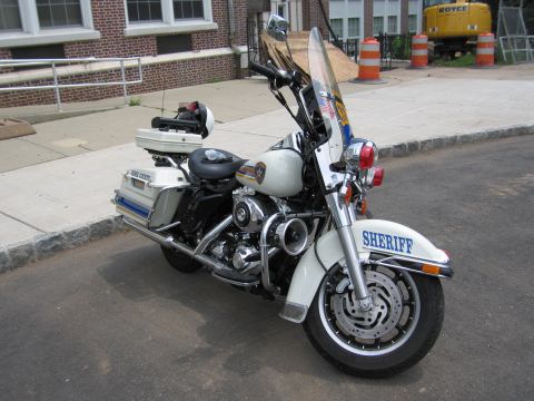 1991 Ford LTD Crown Victoria - white Sheriff police touring motorcycle with windshield, saddlebags and emergency lights, parked at a curb.