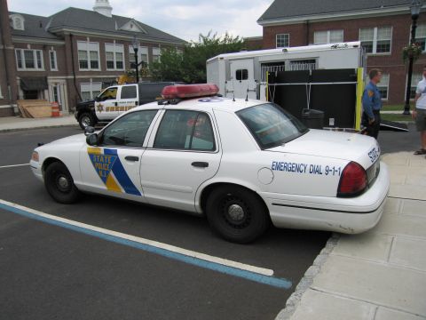 1991 Ford LTD Crown Victoria - Rear driver-side view of a white NJ State Police Ford Crown Victoria sedan parked beside a trailer and a brick building.