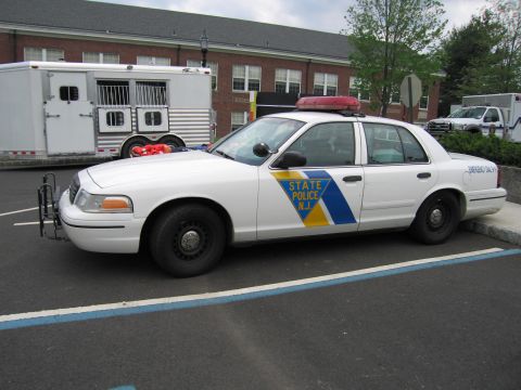 1991 Ford LTD Crown Victoria - Driver-side profile of a white NJ State Police Ford Crown Victoria sedan with blue and yellow chevron striping in a parking lot.