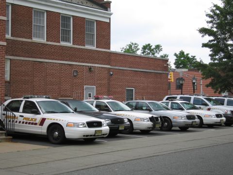 1991 Ford LTD Crown Victoria - row of white police Crown Victoria cruisers parked at an angle along a brick municipal building.