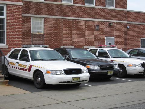 1991 Ford LTD Crown Victoria - white Verona Police Ford Crown Victoria with roof light bar, beside other cruisers at a brick building.