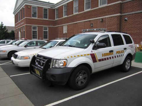 1991 Ford LTD Crown Victoria - white Verona Police Dodge Durango SUV with push bar parked beside Crown Victoria cruisers at a brick building.