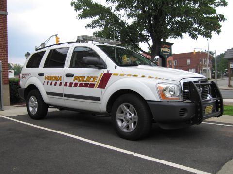 1991 Ford LTD Crown Victoria - Passenger-side front view of a white Verona Police Dodge Durango SUV with push bar and maroon striping at a curb.