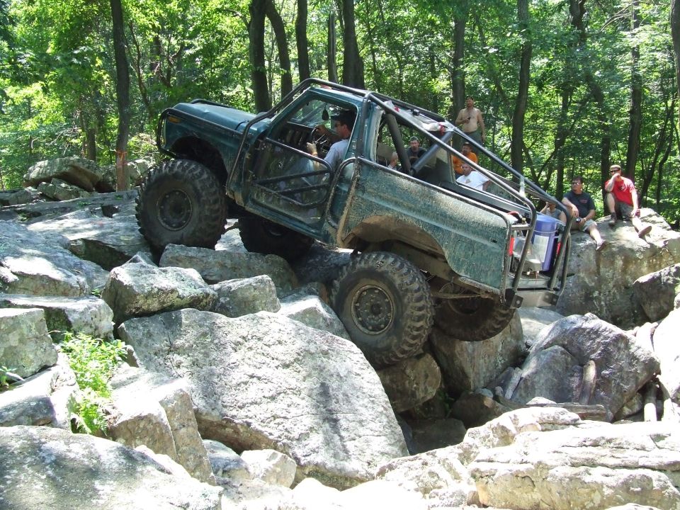 Green 1967 Ford Bronco climbing large rocks on an off-road trail