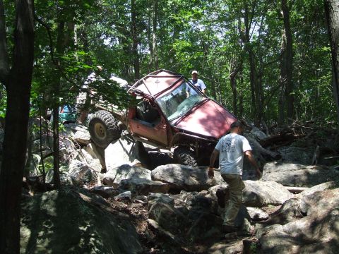 1967 Ford Bronco - Off-road vehicles tackle challenging rocky terrain in a wooded area.