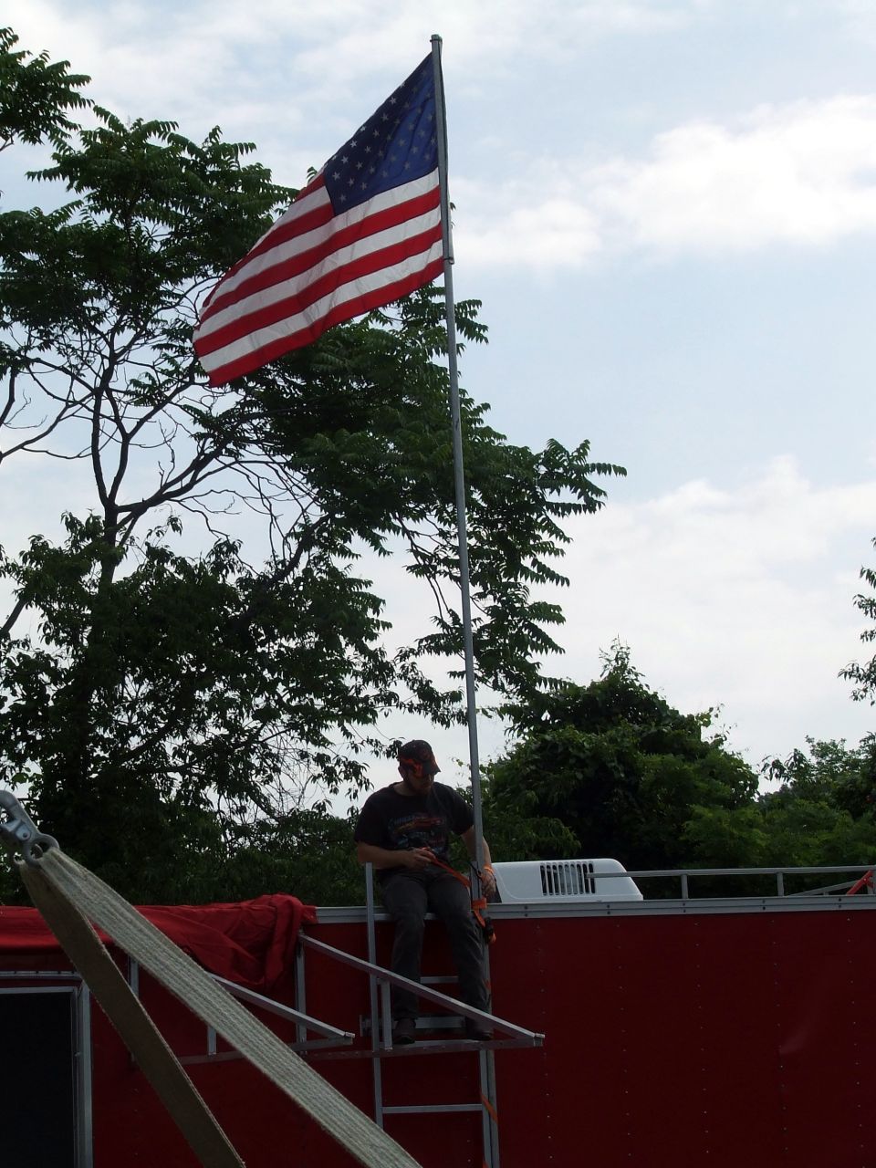American flag waving on a pole, man on platform, trees, Supermotors logo