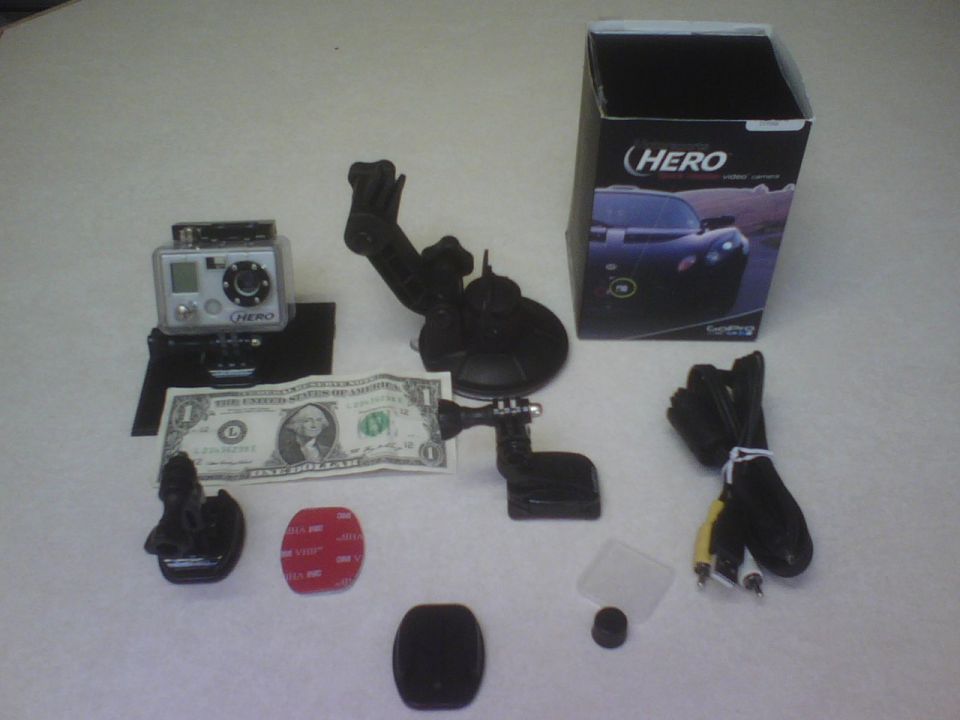 GoPro camera, dollar bill, and various mounting accessories laid out on a white surface