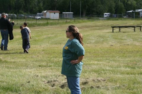 1990 Chevrolet Suburban - A woman stands in a field, with people and buildings in the background.