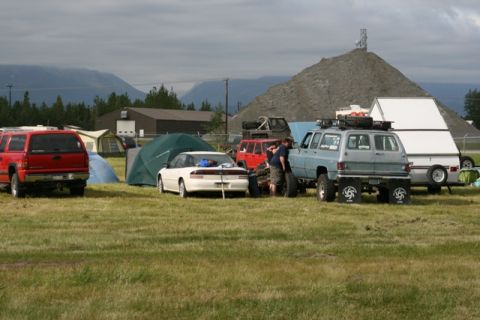 1990 Chevrolet Suburban - A group of vehicles and tents are set up in a field, with a large pile of gravel in the background.