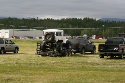 1990 Chevrolet Suburban - Toyota Land Cruiser FJ40 transported on a trailer, with other trucks and an SUV in a grassy field.