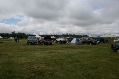 1990 Chevrolet Suburban - A gathering of vehicles and tents in a field on a cloudy day.