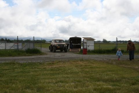 1990 Chevrolet Suburban - A tan off-road vehicle is parked next to an open trailer, with two people walking in the background.