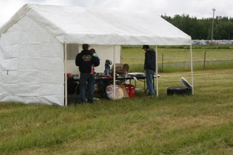 1990 Chevrolet Suburban - People gather under a white tent at an outdoor event, with tables displaying various items.