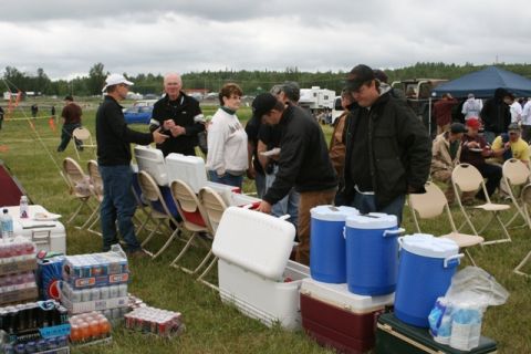 1990 Chevrolet Suburban - People mingle at an outdoor event with an abundance of beverages and coolers set up on the grass.