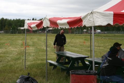 1990 Chevrolet Suburban - An outdoor event is taking place under a large tent with picnic tables and people gathered.
