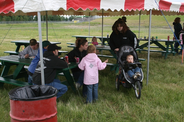 People gathered at picnic tables under a red and white striped tent
