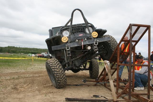Black Jeep Wrangler with smiley face decals on headlights, lifted on a metal ramp