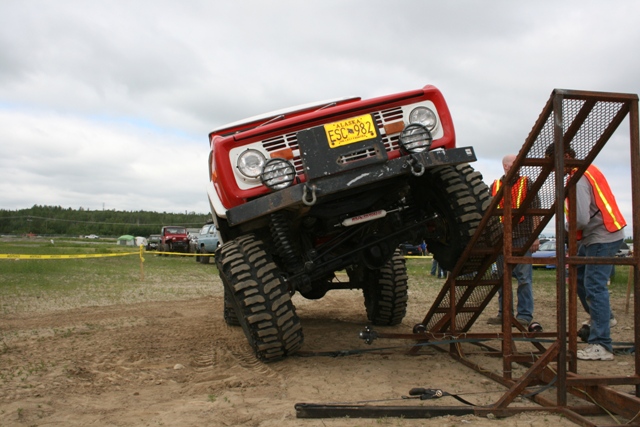 Red off-road vehicle with large tires on a metal ramp, Alaska license plate ESC-982