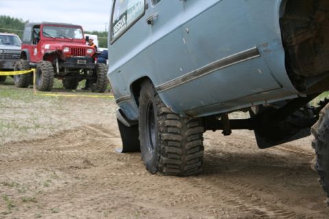 1990 Chevrolet Suburban - A light blue SUV with aggressive off-road tires is parked on a dirt track, with other vehicles visible in the background.