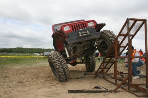 1990 Chevrolet Suburban - A red off-road jeep is shown climbing a metal ramp during an event.