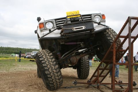 1990 Chevrolet Suburban - An off-road vehicle is positioned on a ramp, with other vehicles and people in the background.