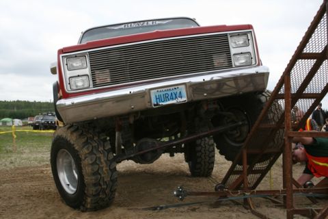 1990 Chevrolet Suburban - This lifted red truck, possibly from the 1980s, features a prominent chrome grille and large off-road tires. Another vehicle is visible in…
