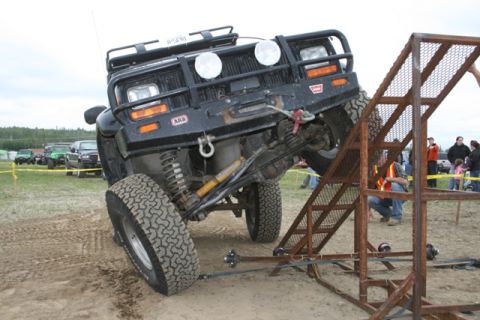 1990 Chevrolet Suburban - A modified black SUV navigates an obstacle course with other vehicles in the background.