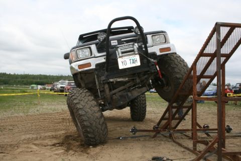 1990 Chevrolet Suburban - An off-road SUV is positioned on a metal ramp, with other vehicles in the background.