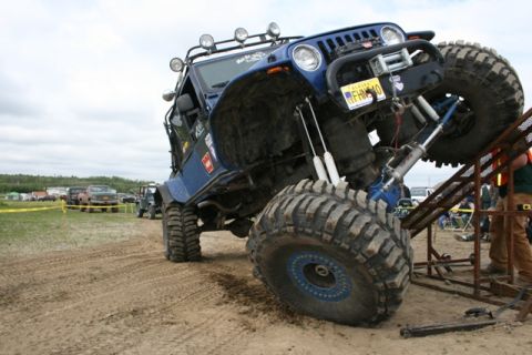 1990 Chevrolet Suburban - A heavily modified blue Jeep Wrangler is shown attempting to climb a ramp during an off-road event.