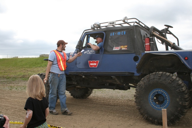 Blue off-road vehicle with large tires and roof rack, driver and passenger visible