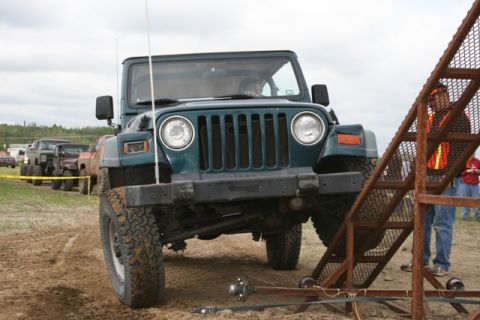 1990 Chevrolet Suburban - A line of off-road vehicles, including a Jeep Wrangler TJ, are parked on a dirt lot.
