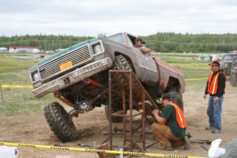 1990 Chevrolet Suburban - A heavily modified pickup truck is elevated on a ramp while two people work on its undercarriage.