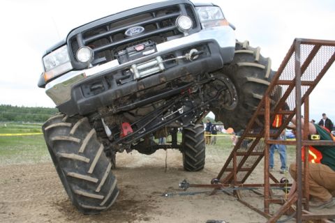 1990 Chevrolet Suburban - Modified Ford truck with oversized tractor tires is positioned near a metal ramp.