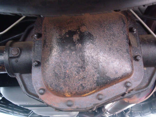Rusty rear differential cover with bolts, viewed from under a vehicle