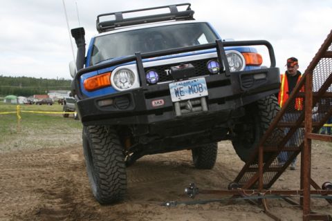1990 Chevrolet Suburban - A blue Toyota FJ Cruiser navigates a sandy obstacle course with a person in an orange vest nearby.